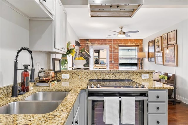 kitchen featuring stainless steel electric range oven, sink, white cabinets, light stone counters, and kitchen peninsula