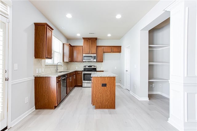 kitchen featuring appliances with stainless steel finishes, decorative backsplash, light stone countertops, a kitchen island, and sink