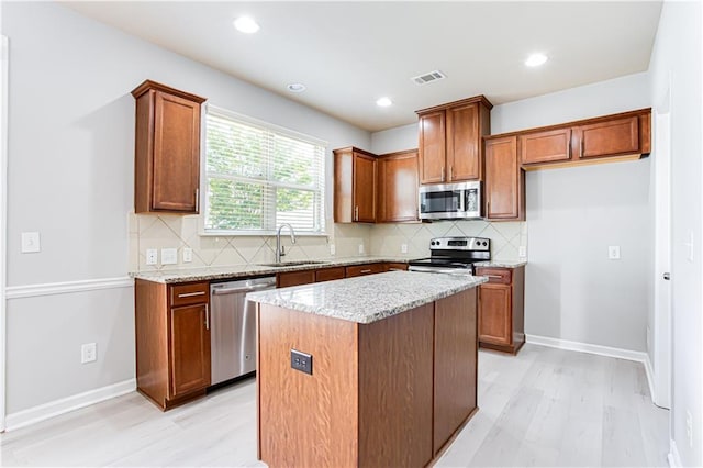 kitchen featuring stainless steel appliances, backsplash, a center island, light stone counters, and sink