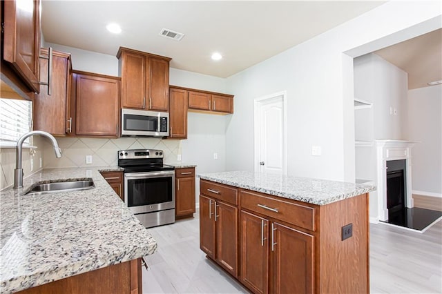 kitchen featuring appliances with stainless steel finishes, a center island, sink, backsplash, and light stone counters