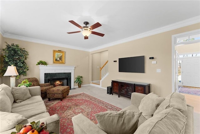 living area featuring stairway, ornamental molding, light carpet, ceiling fan, and a lit fireplace