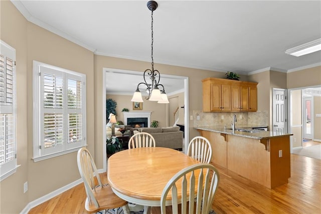 dining room with baseboards, a lit fireplace, light wood-style flooring, and crown molding