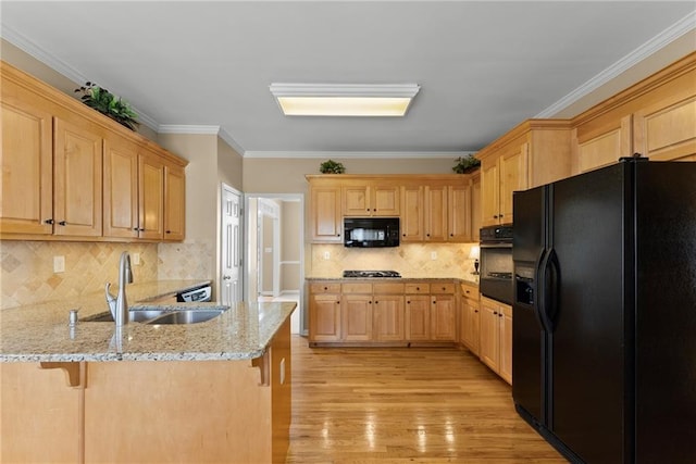 kitchen featuring light brown cabinets, a peninsula, black appliances, light wood finished floors, and a kitchen bar