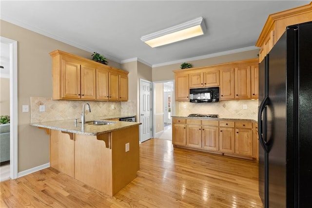 kitchen featuring a peninsula, a sink, light wood-type flooring, light stone countertops, and black appliances