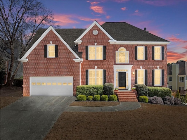 colonial inspired home featuring a garage, driveway, brick siding, and a shingled roof