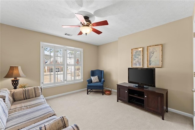 living area featuring light colored carpet, visible vents, a ceiling fan, a textured ceiling, and baseboards