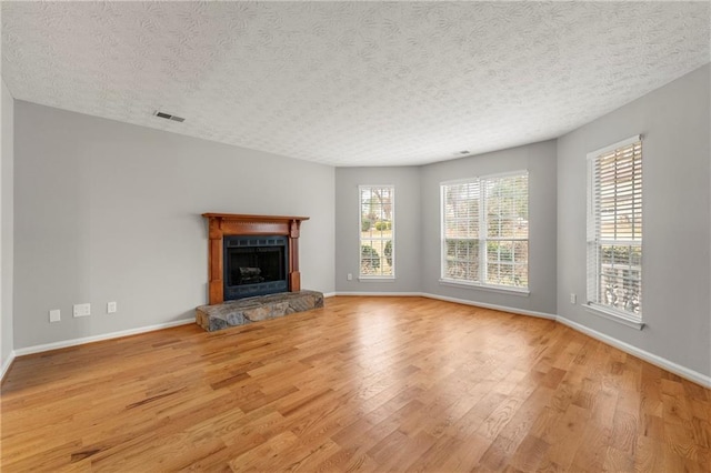 unfurnished living room with a textured ceiling, light wood-type flooring, and a stone fireplace