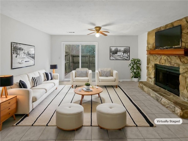 living room with ceiling fan, a stone fireplace, and light tile patterned floors