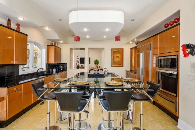 kitchen with built in appliances, backsplash, light tile patterned floors, hanging light fixtures, and a breakfast bar area