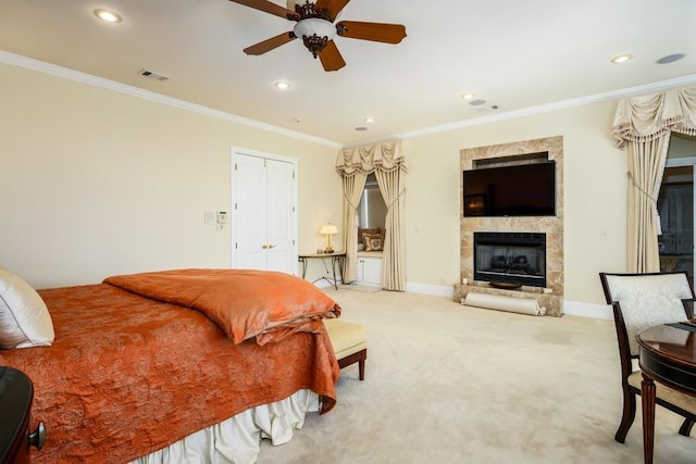 carpeted bedroom featuring ornamental molding, ceiling fan, and a stone fireplace