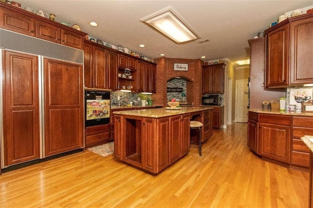 kitchen with a kitchen island, a kitchen bar, light wood-type flooring, light stone countertops, and paneled refrigerator