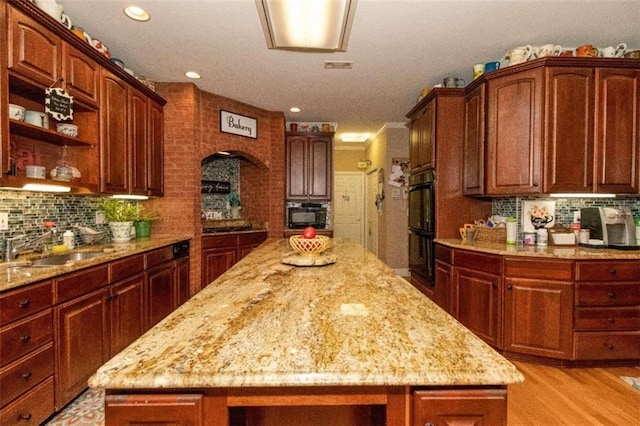 kitchen with tasteful backsplash, light wood-type flooring, light stone counters, and a center island