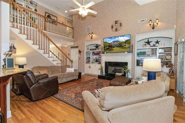 living room with wood-type flooring, a high ceiling, built in shelves, and ceiling fan