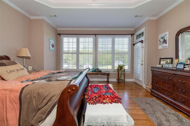 bedroom with hardwood / wood-style flooring, multiple windows, a raised ceiling, and crown molding