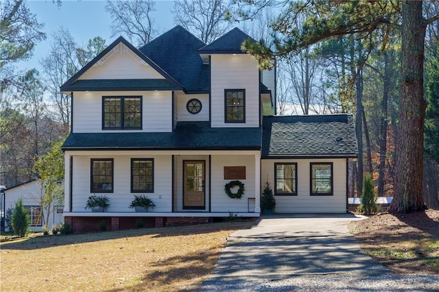 view of front of house featuring driveway, covered porch, a shingled roof, and a front yard