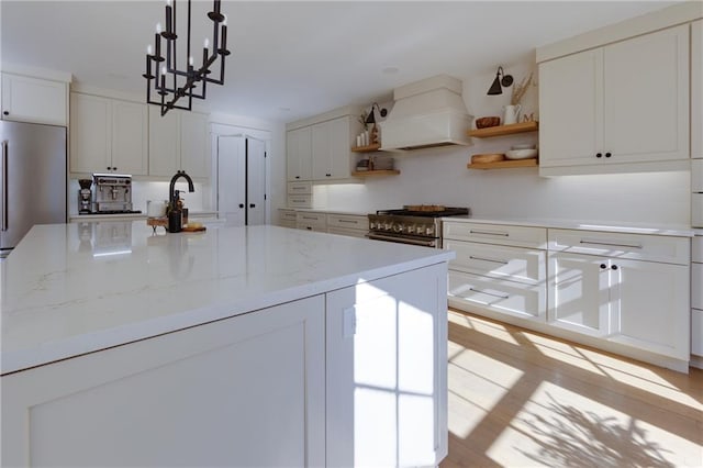 kitchen with light stone counters, high end stove, premium range hood, white cabinetry, and open shelves