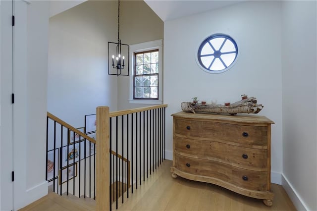 hall with baseboards, a chandelier, wood finished floors, and an upstairs landing