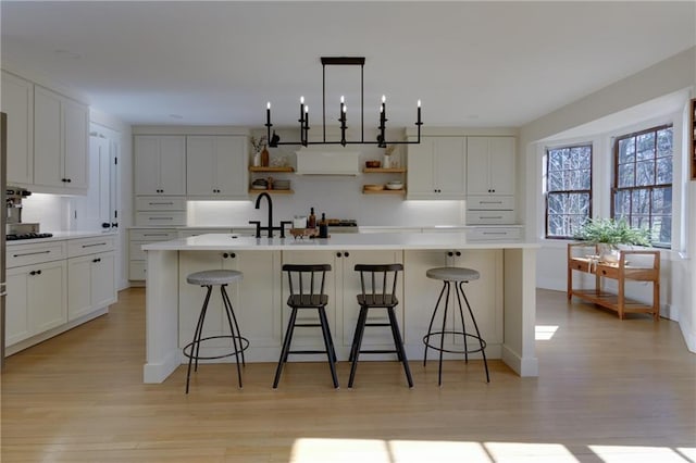 kitchen featuring white cabinets, a center island with sink, and open shelves