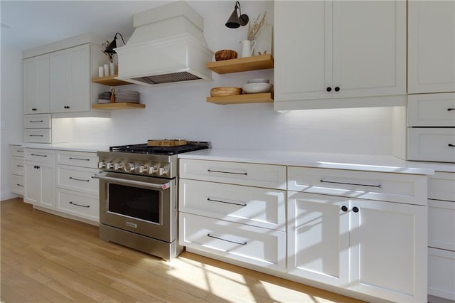 kitchen with open shelves, stainless steel stove, light countertops, light wood-type flooring, and premium range hood