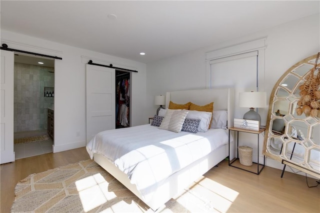 bedroom with a barn door, a closet, wood finished floors, and ensuite bathroom