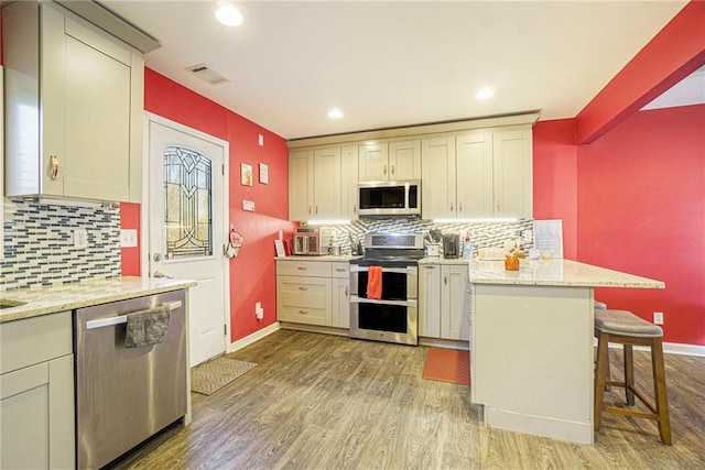 kitchen with a kitchen breakfast bar, kitchen peninsula, stainless steel appliances, light stone countertops, and light hardwood / wood-style floors