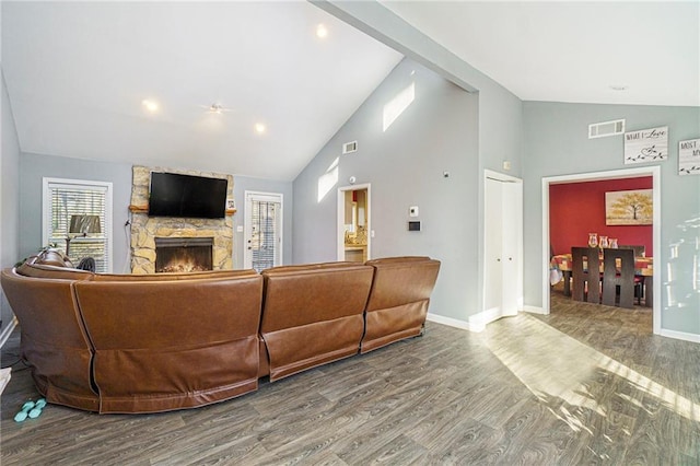 living room with hardwood / wood-style flooring, a stone fireplace, and high vaulted ceiling