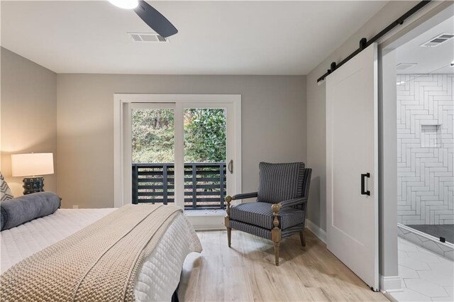 bedroom with light wood-type flooring, ensuite bathroom, ceiling fan, and a barn door