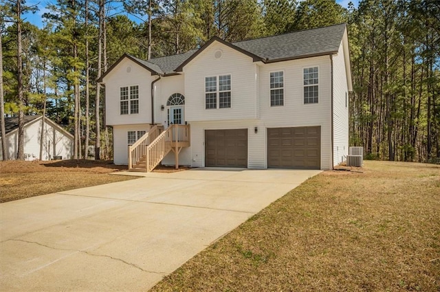 bi-level home with concrete driveway, roof with shingles, a front yard, cooling unit, and an attached garage