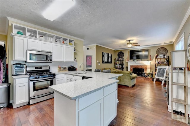 kitchen featuring dark wood-type flooring, white cabinetry, stainless steel appliances, a fireplace, and kitchen peninsula