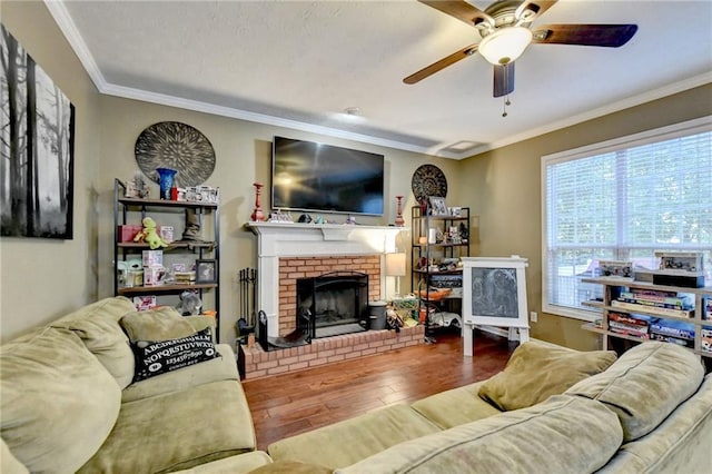 living room featuring a brick fireplace, wood-type flooring, ornamental molding, and ceiling fan