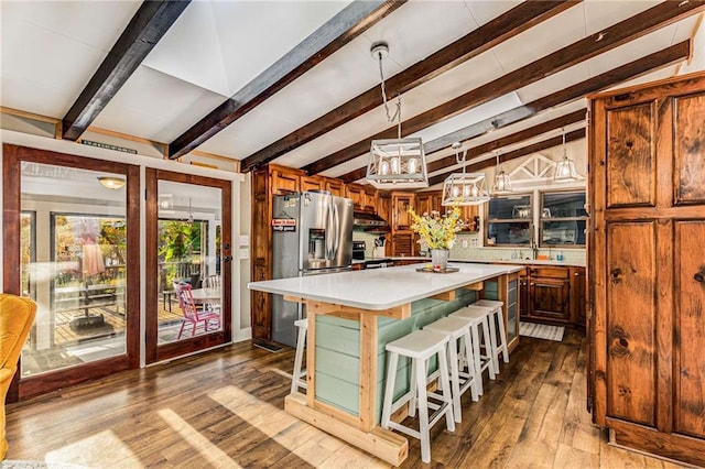 kitchen featuring a center island, stainless steel appliances, vaulted ceiling with beams, hardwood / wood-style floors, and a kitchen bar