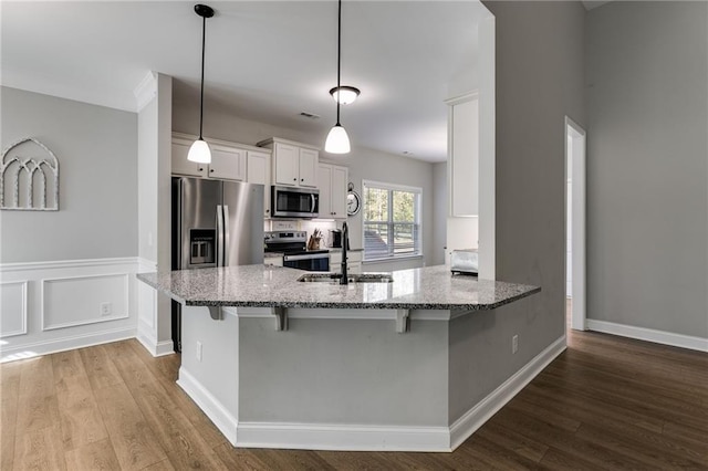 kitchen with pendant lighting, sink, white cabinets, stainless steel appliances, and light stone countertops