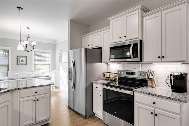 kitchen with light stone counters, ornamental molding, pendant lighting, stainless steel appliances, and white cabinets