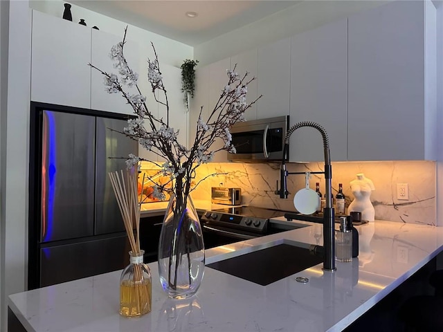 kitchen featuring appliances with stainless steel finishes, light stone countertops, white cabinetry, and backsplash