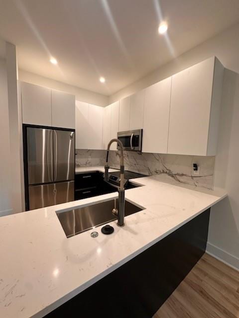 kitchen with white cabinets, sink, light hardwood / wood-style floors, appliances with stainless steel finishes, and backsplash