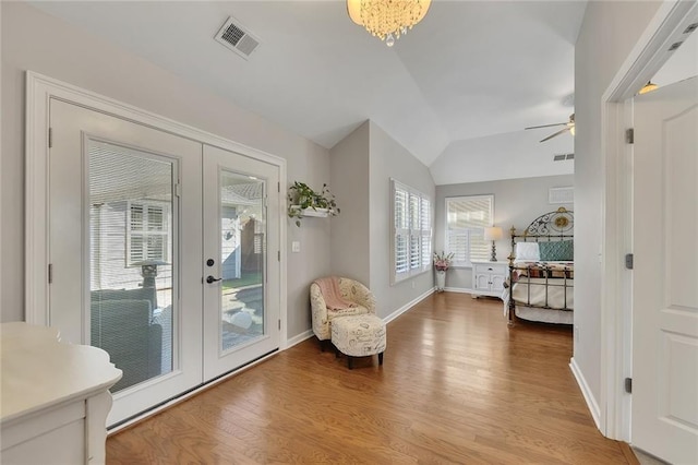 living area with french doors, visible vents, vaulted ceiling, and wood finished floors