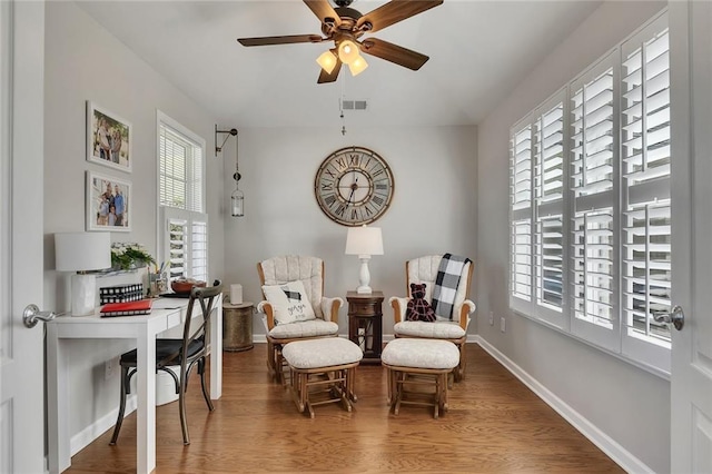 living area with ceiling fan, wood finished floors, visible vents, and baseboards