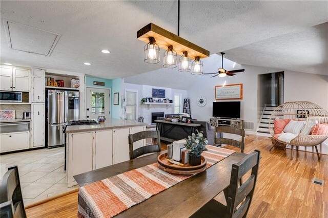 1189 Norfolk Dr NW, Acworth, GA 30102 - dining room with a textured ceiling, light wood finished floors, vaulted ceiling, a fireplace, and a ceiling fan