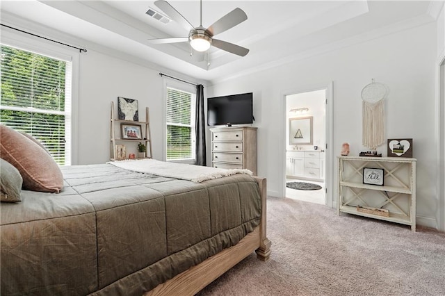 carpeted bedroom with a raised ceiling, crown molding, connected bathroom, and a ceiling fan