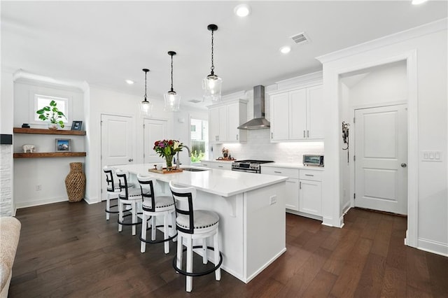 kitchen with wall chimney exhaust hood, stainless steel gas range, a sink, a breakfast bar, and light countertops