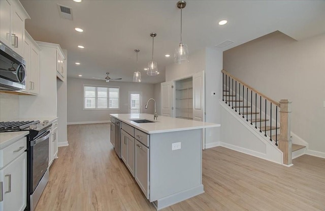 kitchen with sink, appliances with stainless steel finishes, an island with sink, white cabinets, and decorative light fixtures