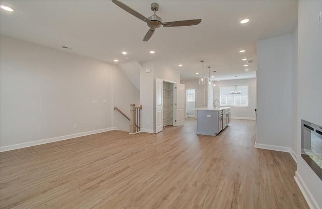 unfurnished living room featuring sink, ceiling fan with notable chandelier, and light hardwood / wood-style floors