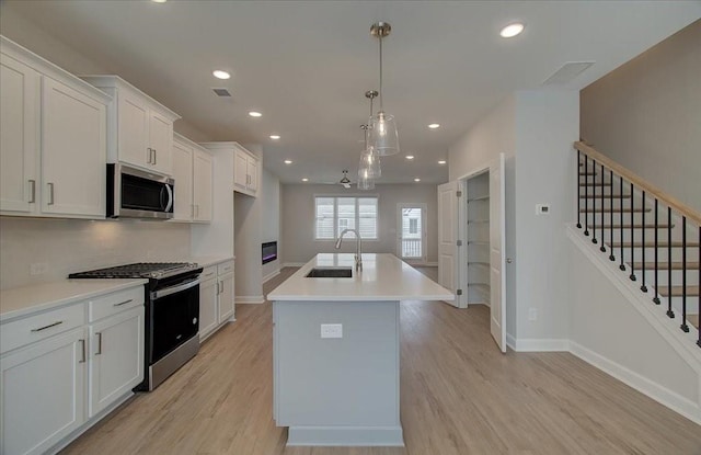 kitchen with pendant lighting, sink, appliances with stainless steel finishes, white cabinetry, and a center island with sink