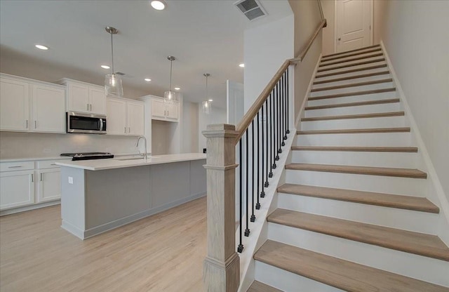 kitchen featuring pendant lighting, an island with sink, sink, white cabinets, and light hardwood / wood-style flooring