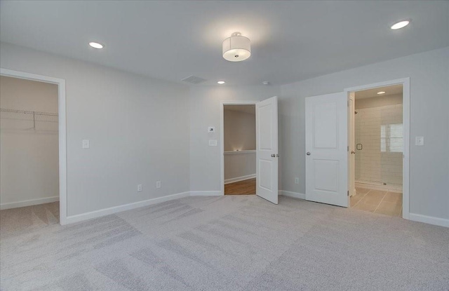 unfurnished bedroom with light carpet, connected bathroom, a walk in closet, and a closet