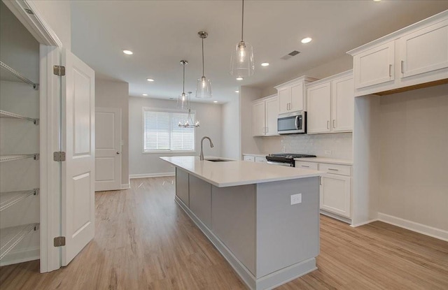 kitchen with stainless steel appliances, a kitchen island with sink, hanging light fixtures, and white cabinets