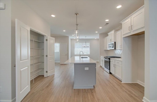 kitchen featuring pendant lighting, white cabinetry, stainless steel appliances, and a kitchen island with sink