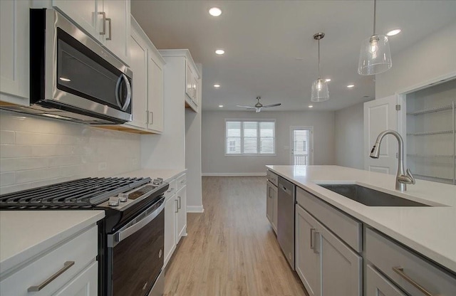 kitchen with pendant lighting, sink, stainless steel appliances, tasteful backsplash, and light hardwood / wood-style floors