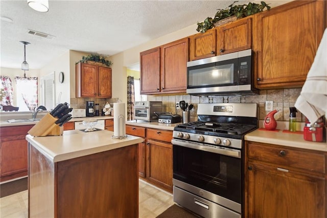 kitchen featuring tasteful backsplash, pendant lighting, a textured ceiling, a kitchen island with sink, and appliances with stainless steel finishes