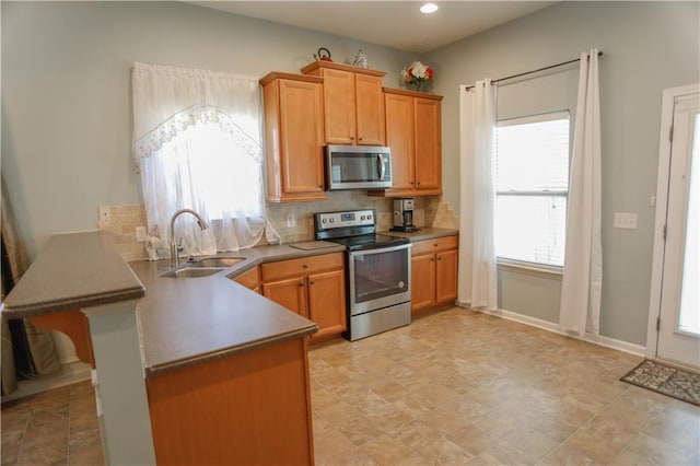 kitchen featuring stainless steel appliances, a peninsula, a sink, backsplash, and brown cabinets